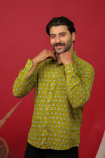 Load image into Gallery viewer, Man wearing an olive green bird printed full sleeve shirt with black jeans against a red background.