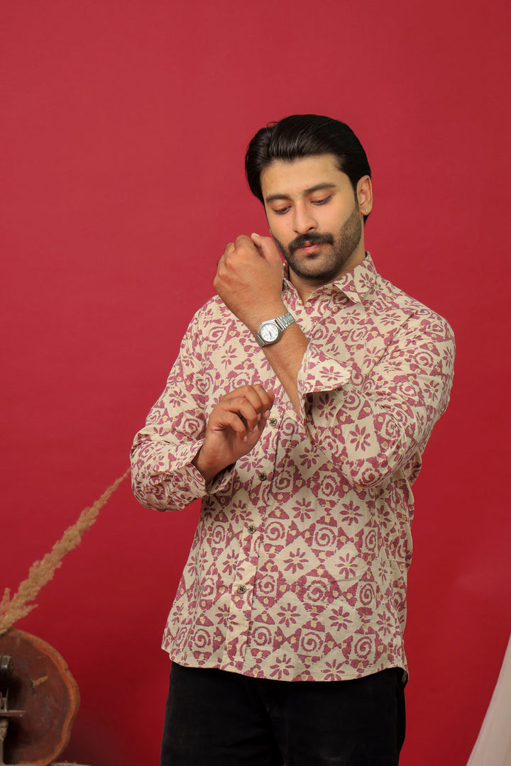 Man wearing a beige abstract printed full sleeve shirt with black jeans against a red background.
