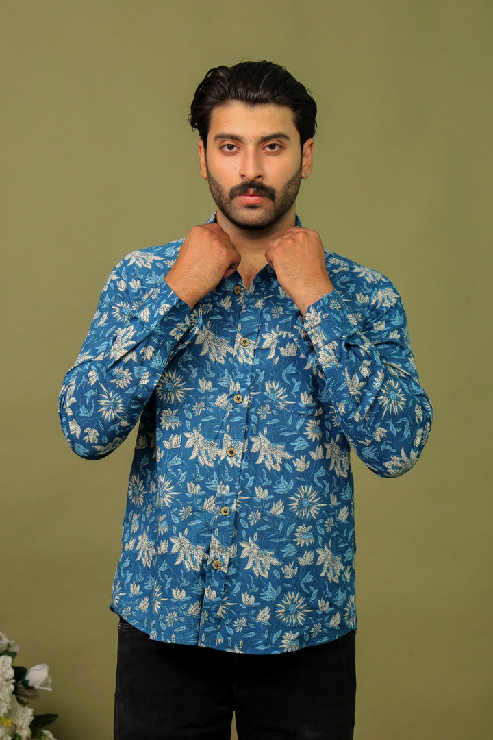 Man wearing a blue tropical floral printed full sleeve shirt with black jeans against an olive green background.