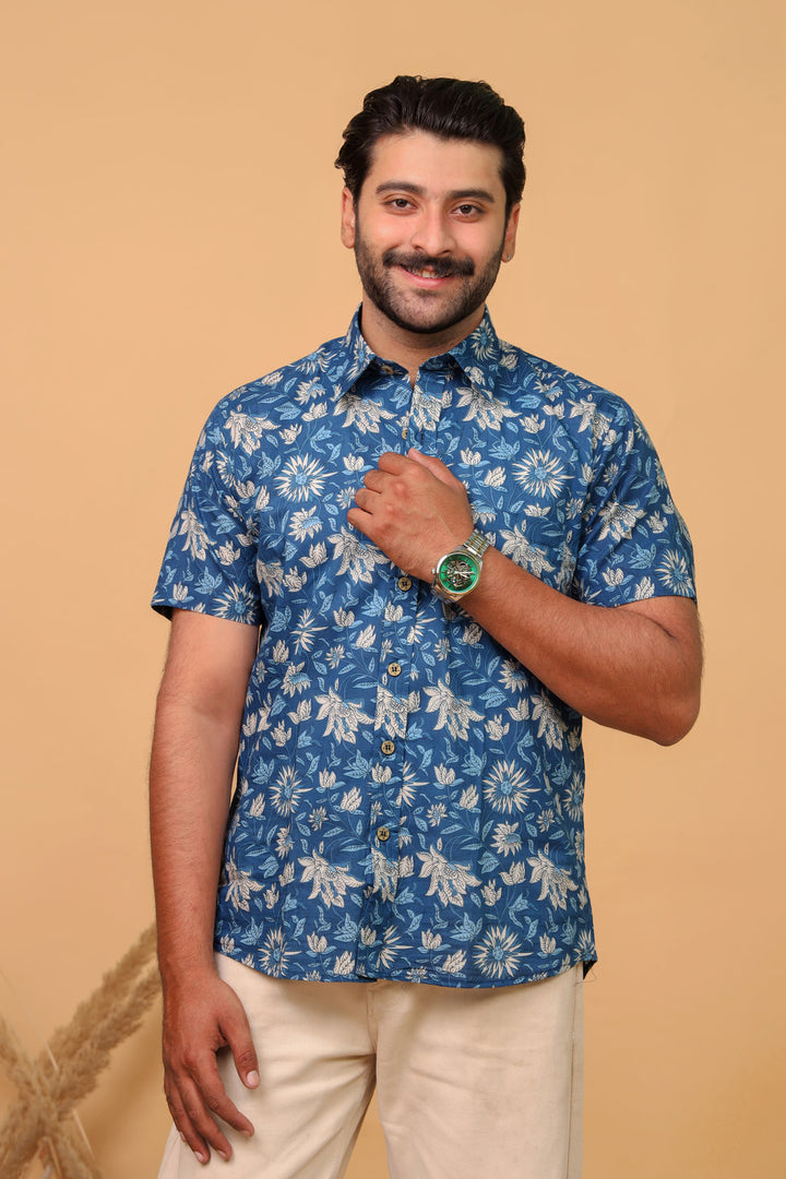 Man wearing a blue tropical floral printed half sleeve shirt with beige trousers against a beige background.