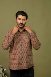 Man wearing a brown floral printed full sleeve shirt with black jeans against an olive green background.