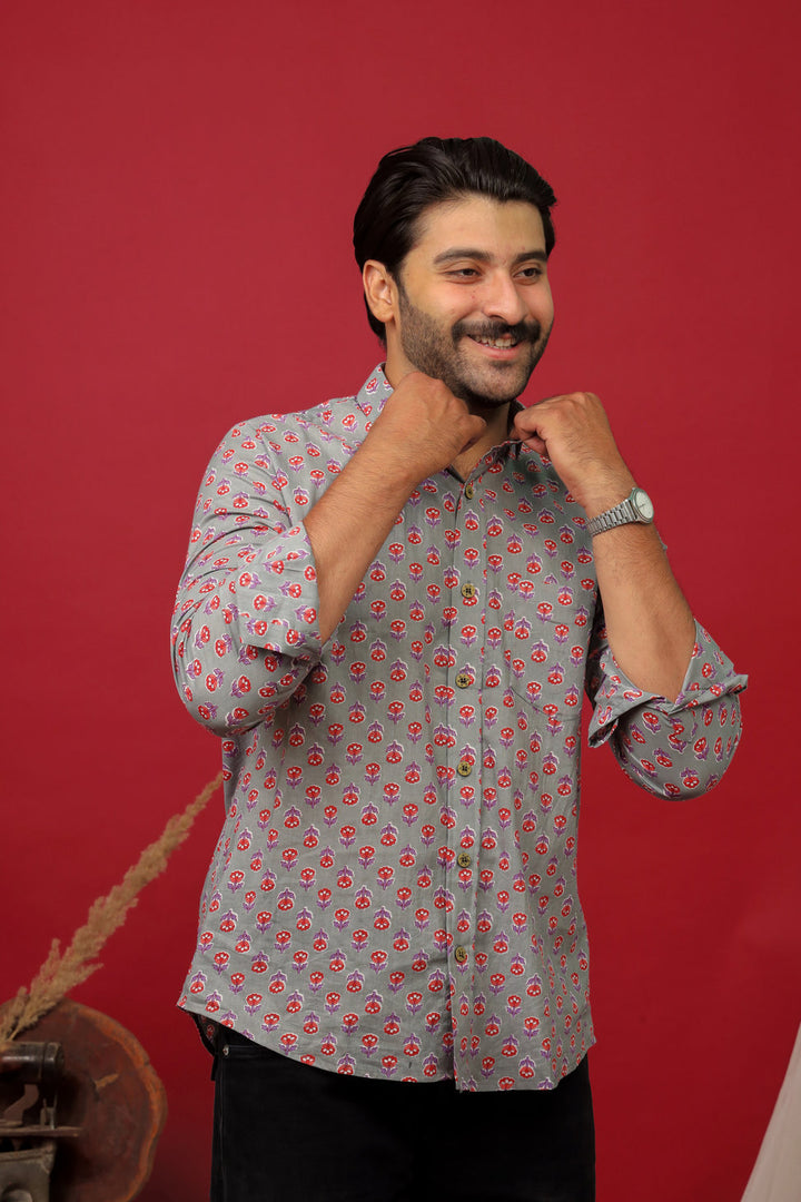Man wearing a grey floral printed full sleeve shirt with black jeans against a red background.