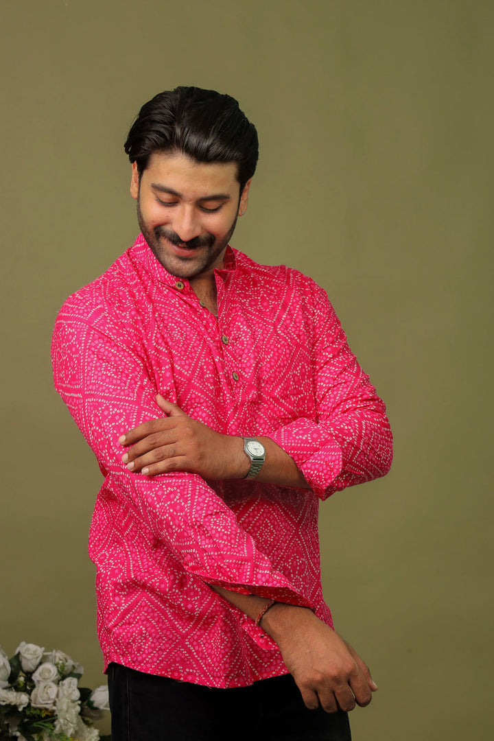 Man wearing a hot pink Bandhani printed kurta shirt with black jeans against an olive green background.