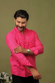Man wearing a hot pink Bandhani printed kurta shirt with black jeans against an olive green background.