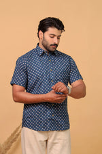 Load image into Gallery viewer, Man wearing a navy blue floral printed half sleeve shirt paired with beige trousers on a plain beige background.