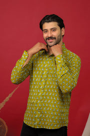 Man wearing an olive green bird printed full sleeve shirt with black jeans against a red background.