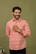 Load image into Gallery viewer, Man wearing a peach floral printed full sleeve shirt with black jeans against an olive green background.