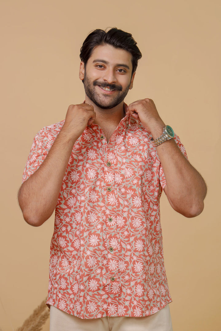 Man wearing a peach floral printed half sleeve shirt with beige trousers against a beige background.