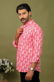 Man wearing a pink leaf printed kurta shirt with black jeans against an olive green background.