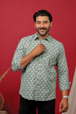 Load image into Gallery viewer, Man wearing a sage green floral printed full sleeve shirt with black jeans against a red background.