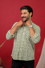 Load image into Gallery viewer, Man wearing a sage green paisley printed full sleeve shirt with black jeans against a red background.