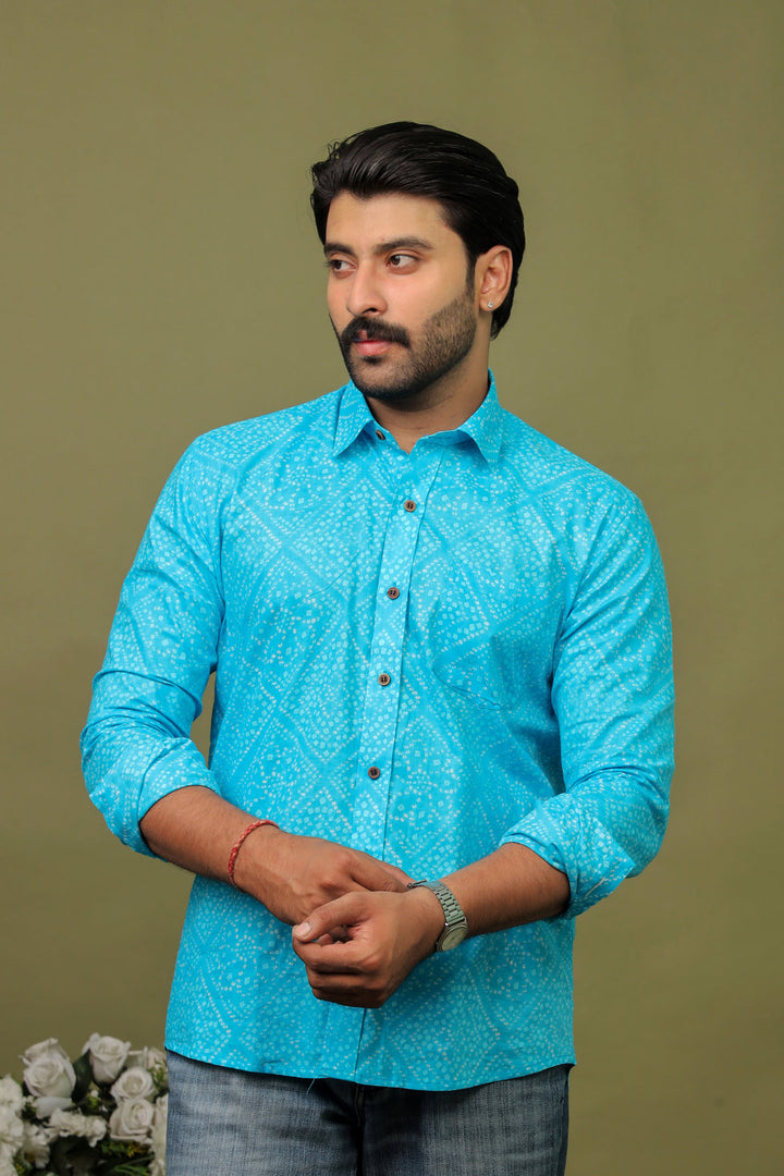 Man wearing a sky blue cotton shirt with subtle white Bandhani print and light denim jeans against an olive green background.