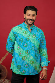 Man wearing a sky blue Bandhani printed kurta shirt with black jeans against a red background.