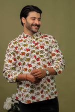 Load image into Gallery viewer, Smiling man wearing a white cotton shirt with colorful elephant print and black jeans against an olive green background.