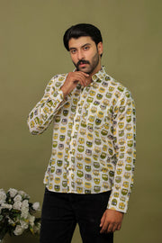 Man wearing a white cotton shirt with green and yellow owl print paired with black jeans against an olive green background.