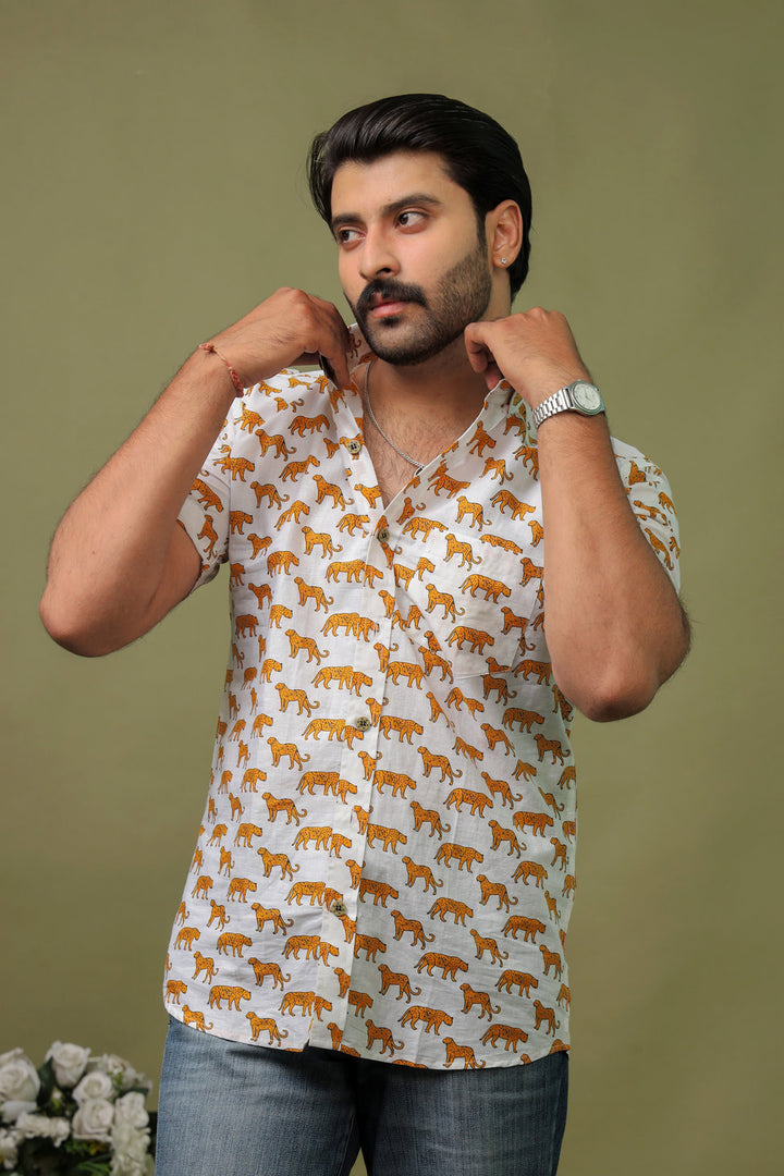 Man wearing a white cotton shirt with orange tiger print and denim jeans against an olive green background.